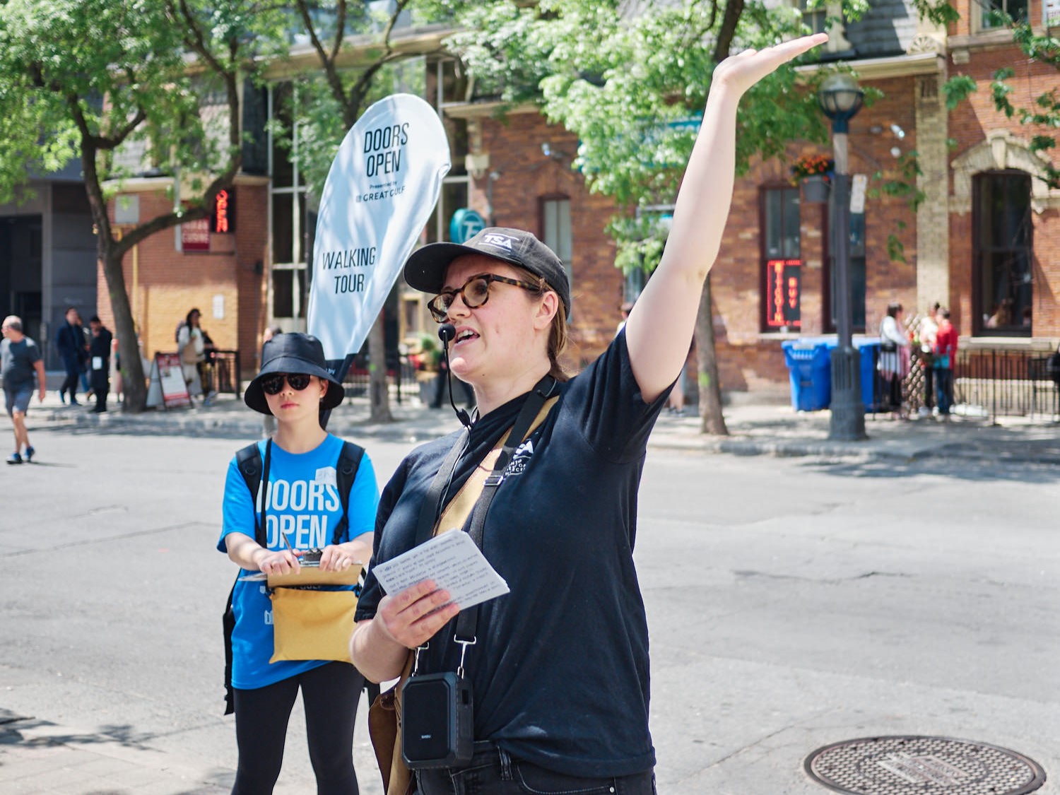 Tour Guide leading a tour with her arm raised high in reference to one of the buildings.